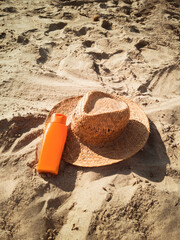 Crema solar en la arena playa junto a un sombrero de paja. Vista superior