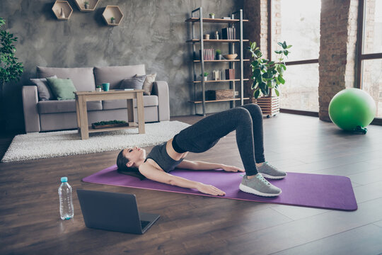 Full length photo of active athlete energy endurance intense beautiful girl watch video laptop doing pilates aerobics plank in mat floor stretch abdomen stomach back in house indoors