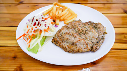 Pork steak with French fries and salad  in a white plate on a wooden table