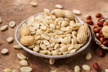 Peanuts peeled and in shell, in ceramic plate, brown background, close up.