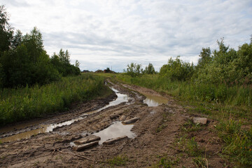 a bad muddy countryside off road with big puddles, dirt and tire tracks after a heavy rain and a cloudy blue sky in the background. Ivanovo, Vladimir Oblast, Russia