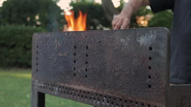 un homme pr&eacute;pare des grillades dans un barbecue en fer forg&eacute;.