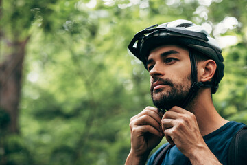 Closeup portrait of sporty young man close the protective helmet and looking away, posing on nature...