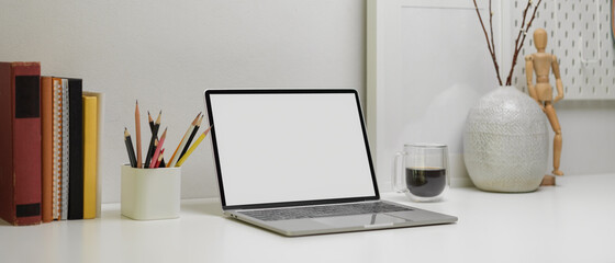 Modern office desk with mock-up laptop, stationery, books, coffee mug and decorations