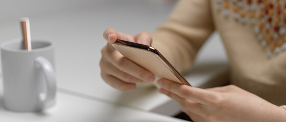 Female hands holding smartphone while sitting at white office desk