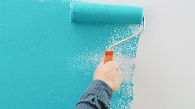 Man painting wall with blue paint using roller. Construction worker, tool, apartment renovation.
