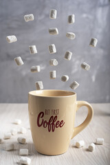Obraz na płótnie Canvas Beige cup of coffee with lettering standing on light wooden table with white flying marshmallows at kitchen