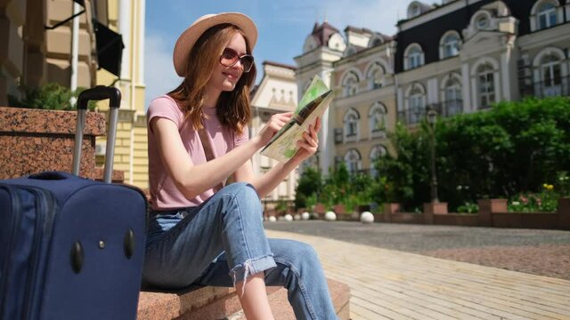 Beautiful Young Woman tourist Pleasant with city map and suitcase sitting on stairs