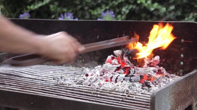Une homme renue les braises dans un barbecue en fer forg&eacute;.