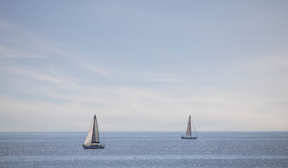 Two sail boats drifting over the ocean in front of a wispy blue sky. © Global News Art