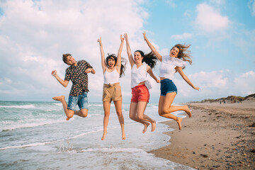 friends jump together on the beach near the sea on a summer day. They are 4, laugh and have fun