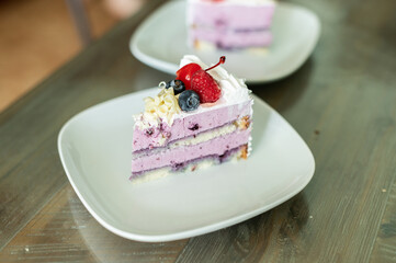 a beautiful delicious piece of cake is on a white plate, the cake is decorated with white chocolate chips, strawberry slices, raspberries, blueberries, cherries, with a whipped white cream.