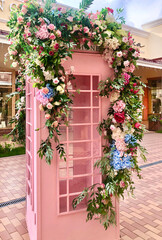 Fototapeta na wymiar A beautiful telephone box stands on the street. Decorated with beautiful flowers roses, hydrangea, greenery. Beautiful decoration of a bouquet of flowers