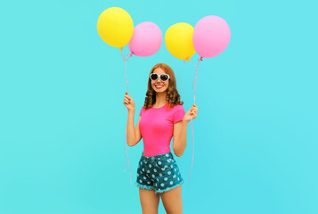 Summer colorful cheerful image of happy smiling young woman with yellow pink balloons having fun wearing a shorts and straw hat on blue wall background