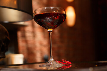 detailed closed drink shot of a delicious fresh dark red cosmopolitan cocktail in a transparent glass standing on a table on a red brick dark background