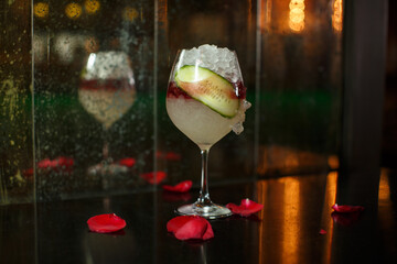 close up drink shot of a delicious fresh yellow red cocktail with ice, a cucumber slice in a...