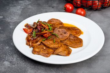 Beef tongue with sauce and vegetables on a white plate