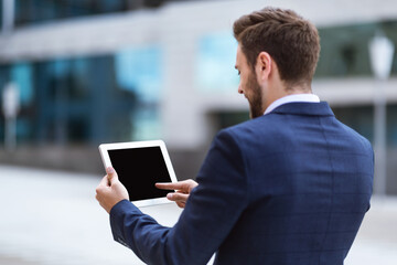 Business executive holding tablet computer with blank screen near office building, mockup for design