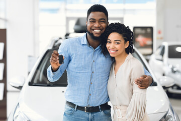 Couple Holding New Automobile Key Embracing Near Car In Dealership