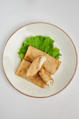 Pancakes with curd filling lie on a white plate with green salad. White background. Russian traditional cuisine.