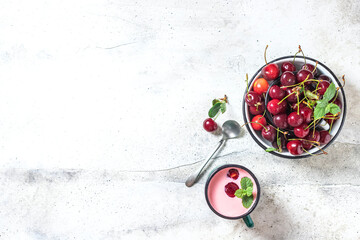 Yogurt with cherry, mint and and fresg berries on a light concrete background. Summer healthy dessert with berries.