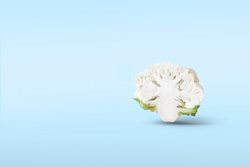 One Half a head of cut cauliflower closeup levitate in the air on a blue background with a shadow. Creative flying food concept.Minimalistic vegetable background with copy space for text.
