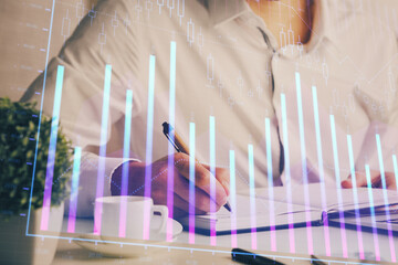 Double exposure of man's hands writing notes of stock market with forex chart.