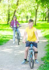 Young boy and her mother stand with bicycles in a sunny summer park