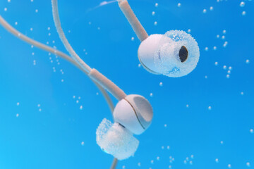 Headphones under water on blue background. Listening to music, waterproof accessory