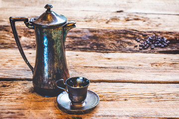 Vintage photo a silver coffee pot and a silver espresso cup on wooden table.