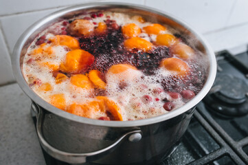 Fresh fruits are boiled in boiling water in a metal pan on the stove. Delicious stewed apricot, apples, cherries, raspberries. Photography, concept.