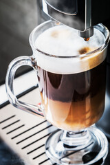 glass cup with hot cappuccino with foam prepared in the coffee machine