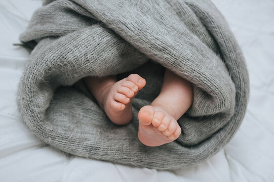 A small child sleeps on a white bed, covered with a gray plaid close-up. The legs of the newborn. Photography, concept.
