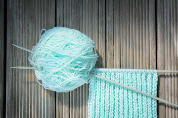 Knitting needles stuck in a toll of yarn with knitwork in progress on wooden background.