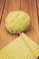 Retro-style photo of a woolen yarnroll, knitting needles, and knitwork in progress on wooden background.