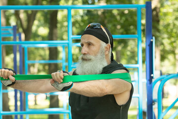 Old man doing fitness exercises with elastic resistance band.Bearded senior training with rubber band. Workout ,sports, healthy lifestyle concept.