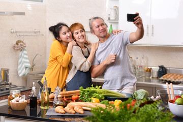 Happy family of mother father and daughter cooking in kitchen making healthy food together and using smart phone to take selfies