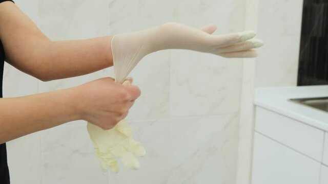 Caucasian young women dental doctor putting on rubber white gloves on her hands in hospital or clinic. Side view.