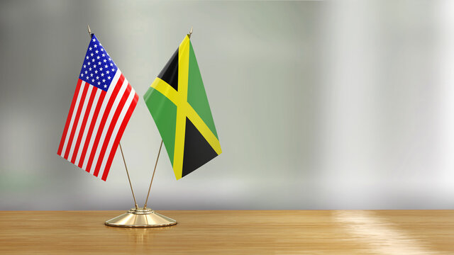 American And Jamaican Flag Pair On A Desk Over Defocused Background 