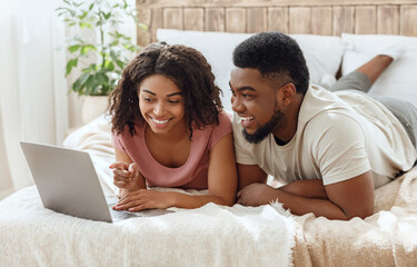 Laughing black couple watching funny content on laptop