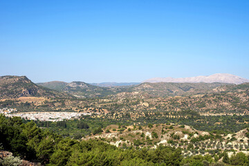 Rhodes island scenery on a sunny summer day with dry trees, fields, brown soil and blue clear sky with haze
