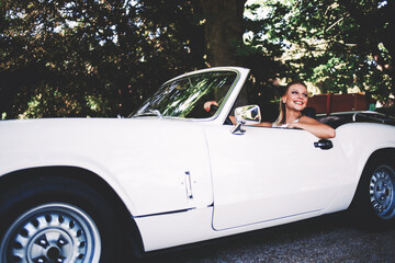 Successful and wealthy woman sitting behind the wheel of her luxury cabriolet car on countryside feeling happy,young smiling female sits in her new convertible car outdoors enjoying the life in summer
