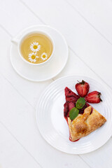 Freshly baked homemade galette or open strawberry pie and fresh mint leaves with a cup of chamomile herbal tea, summer food. Soft selective focus.