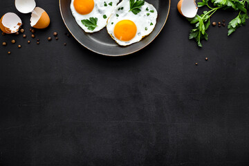 Fried eggs on frying pan on black desk top-down copy space