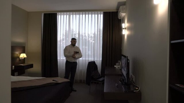 Mature businessman in a hotel room gets dressed and watches TV.