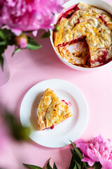 Top view of piece of cherry pie with peonies flowers on a pink background