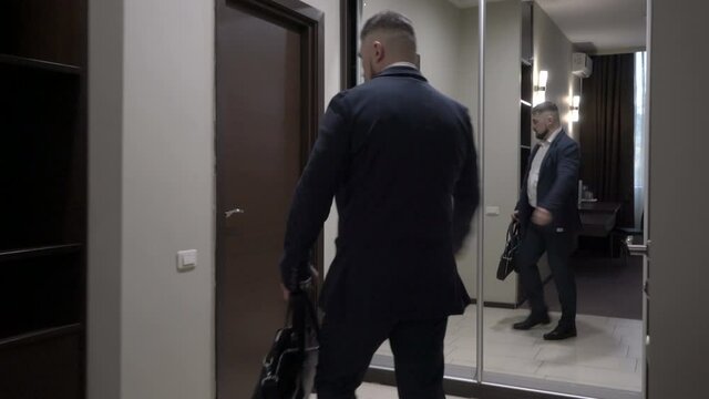 Mature businessman leaves a hotel room turning off the light.