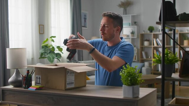 A handsome young man takes a camera out of a cardboard box. Unpacking online purchases.
