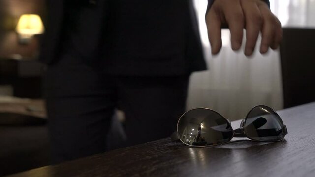 Mature businessman leaves the hotel room, picking up glasses from the table.