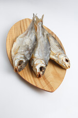 close up top view shot of three Russian dried salted vobla (Caspian Roach) fish on a wooden plate on a white background